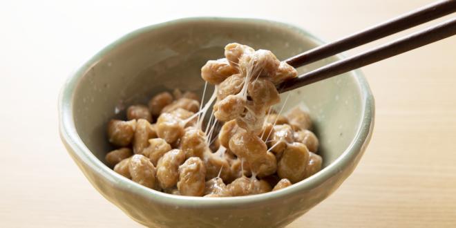 Chopsticks picking up some natto from a small bowl.